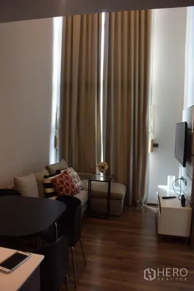 公寓 出租在Watthana, Bangkok - 客厅挑高，落地窗帘与小型沙发，空间明亮舒适。