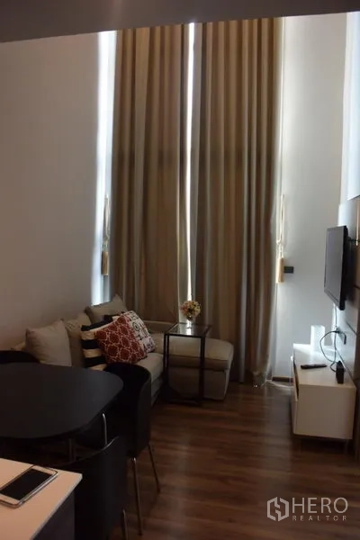 公寓 出租在Watthana, Bangkok - 客厅挑高，落地窗帘与小型沙发，空间明亮舒适。
