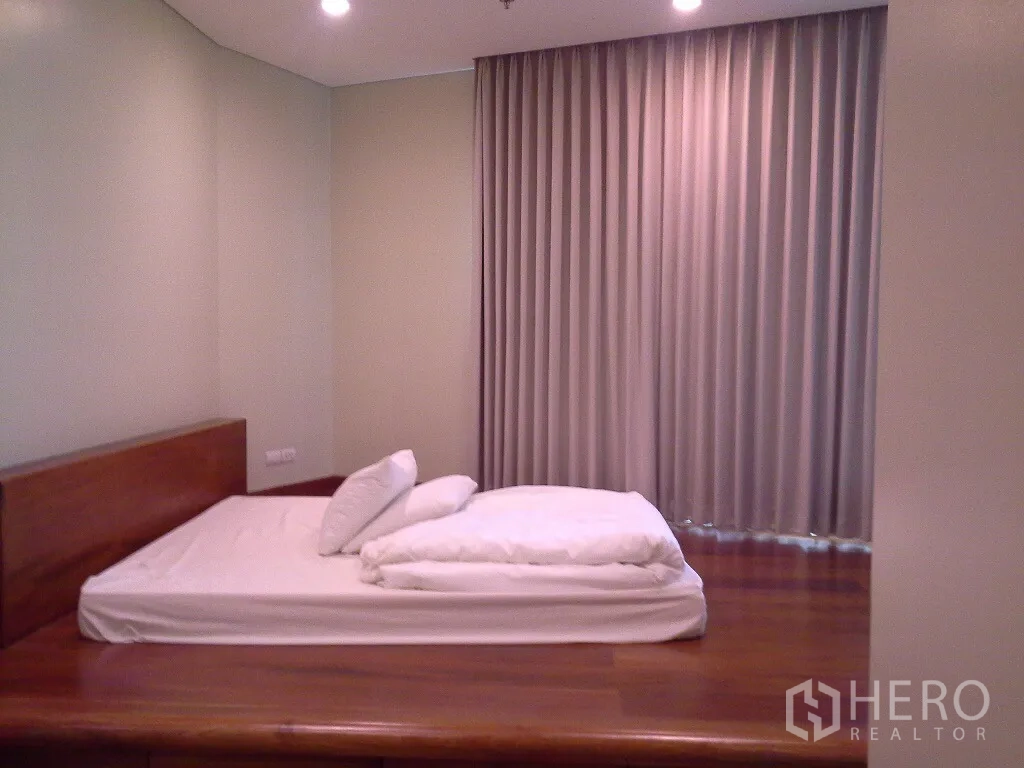 Condominium for rent or sale in Khlong Toei, Bangkok - Cozy bedroom with a wooden platform bed, recessed lighting, and full-length curtains.