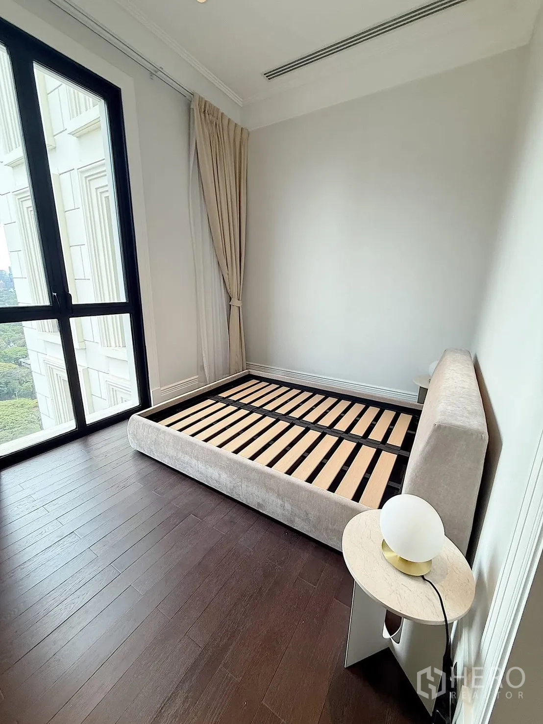 คอนโด for rent or sale in Pathum Wan, Bangkok - ห้องนอนที่สองมีเตียงเตี้ย โต๊ะข้างเตียง และหน้าต่างสูงมองเห็นพื้นที่สีเขียว