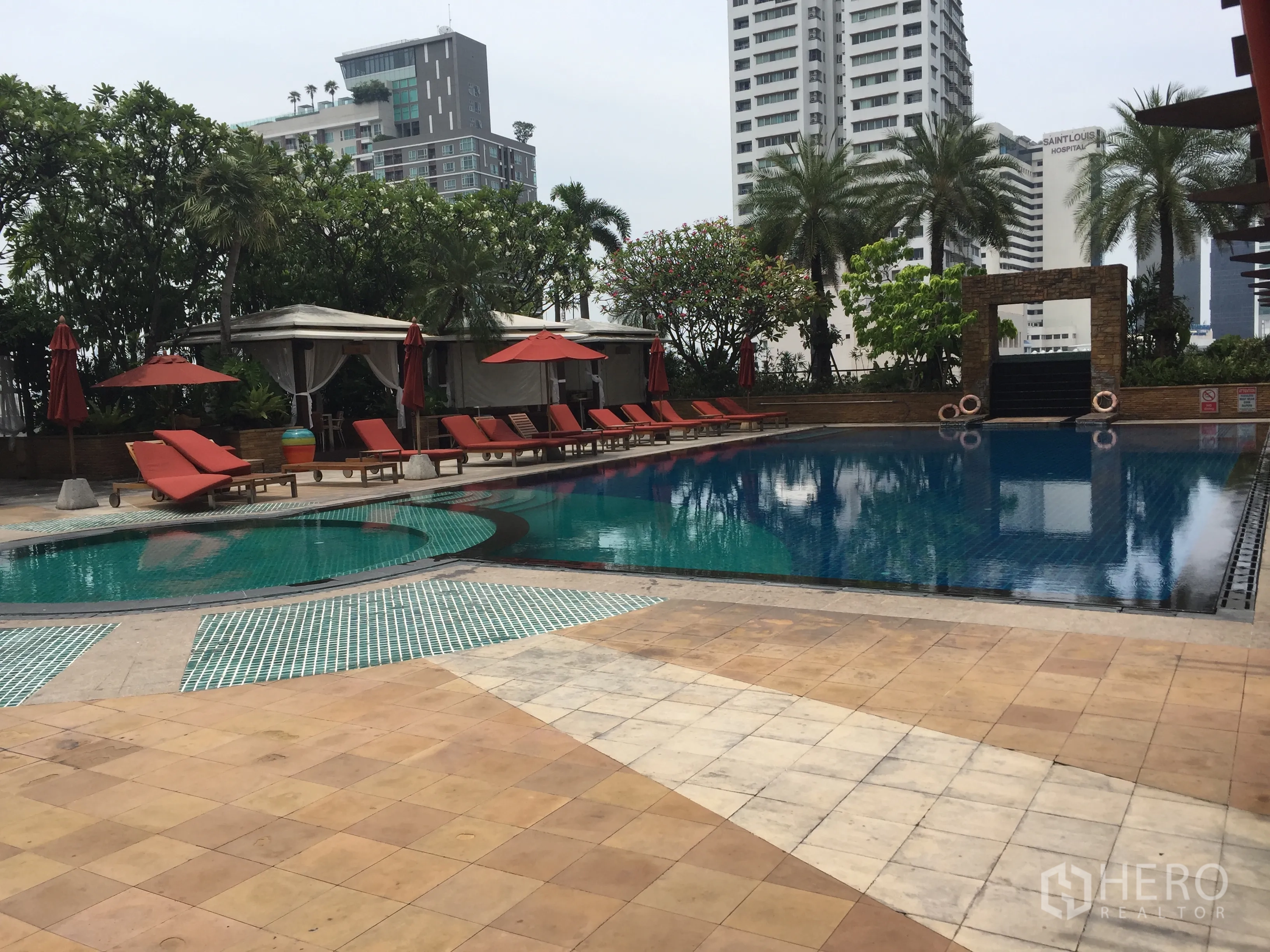 Condominium for rent in Sathon, Bangkok - Outdoor swimming pool with sun loungers and cabanas surrounded by palms and city views.