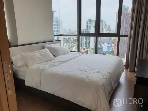 公寓 出租在Watthana, Bangkok - 转角卧室，整面落地窗俯瞰城市天际线，配大床与白色床品。