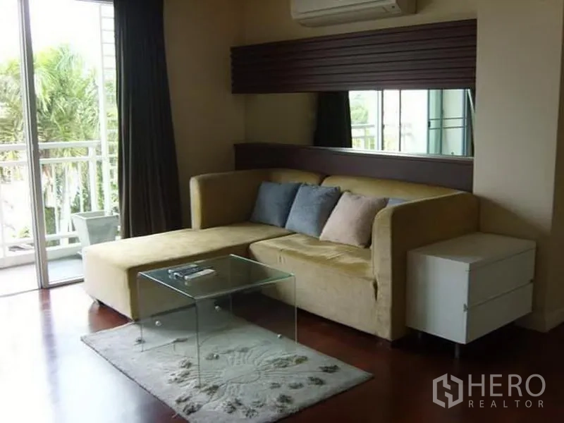 Condominium for rent in Watthana, Bangkok - Living area with sectional sofa, rug and sliding door opening to a balcony.