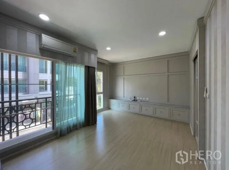 Townhouse for sale - Spacious living room with balcony access, air-conditioner, wood floors, and built-in low cabinets.