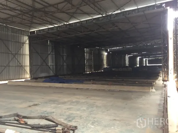 Warehouse for rent in Mueang Pathum Thani, Pathum Thani - Spacious warehouse interior with steel truss roof, concrete floor, and natural side lighting for storage.