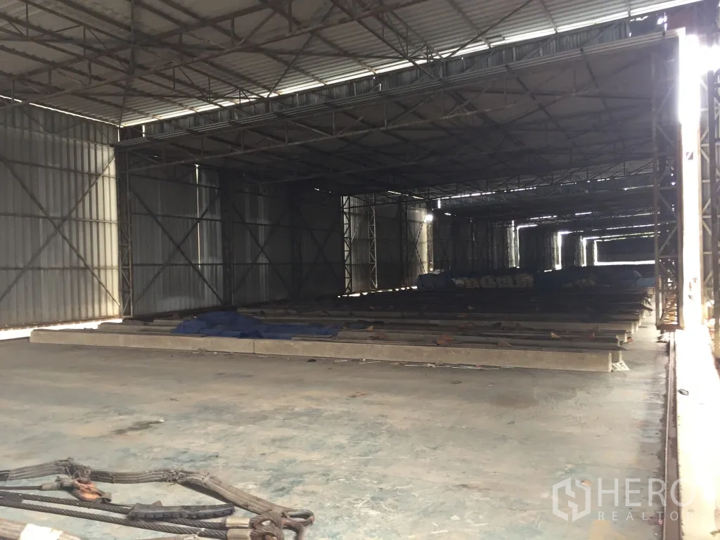 Warehouse for rent in Mueang Pathum Thani, Pathum Thani - Spacious warehouse interior with steel truss roof, concrete floor, and natural side lighting for storage.