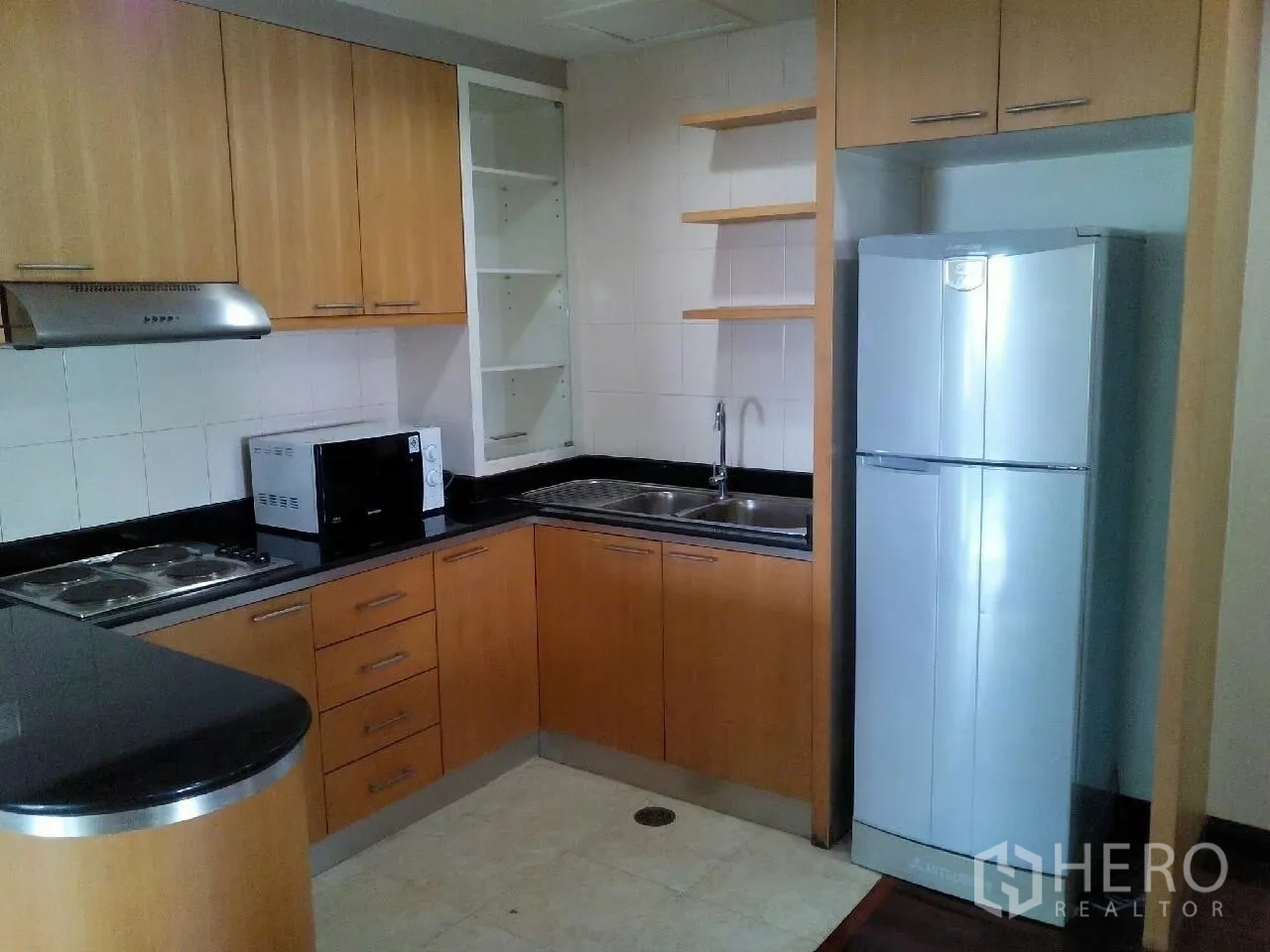Condominium for rent in Phaya Thai, Bangkok - L-shaped kitchen with wood cabinetry, black countertops, cooktop, range hood, microwave and a stainless refrigerator.