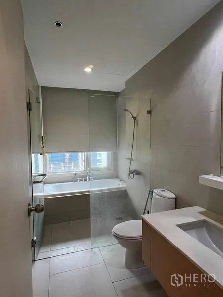 Condominium for rent in Ratchathewi, Bangkok - Second bathroom featuring a bathtub by the window, glass partition, and vanity.