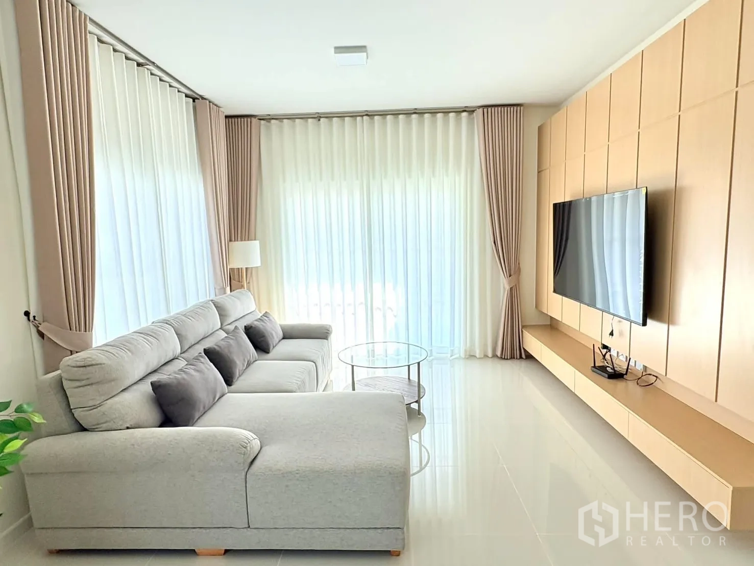 บ้าน for rent in Bang Phli, Samut Prakan - มุมห้องนั่งเล่นโชว์ผนังทีวี โซฟาตัวใหญ่ และผ้าม่านสูงเต็มบาน
