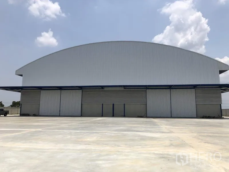 Factory for rent or sale in Lat Lum Kaeo, Pathum Thani - Modern high-span factory with arched roof, multiple sliding doors and a vast concrete yard under a clear sky.