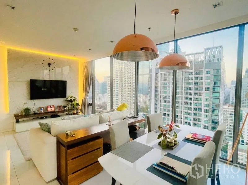 Condominium for rent or sale in Sathon, Bangkok - Dining table under copper pendant lights beside floor-to-ceiling windows.