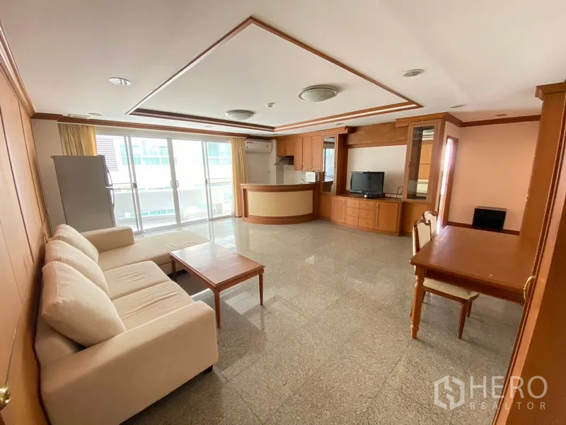 房间 出租在Watthana, Bangkok - 宽敞客厅，整面推拉玻璃门通向阳台，配备一体化厨房与书桌。