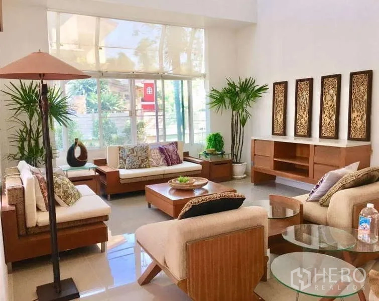 Detached House for rent in Lat Krabang, Bangkok - Airy living room with tall windows, neutral sofas and wooden furniture.
