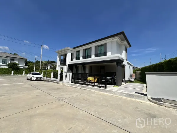 独立式住宅 出租或出售在Mueang Pathum Thani, Pathum Thani - 街角视角的白色两层住宅，宽阔车道与车库。