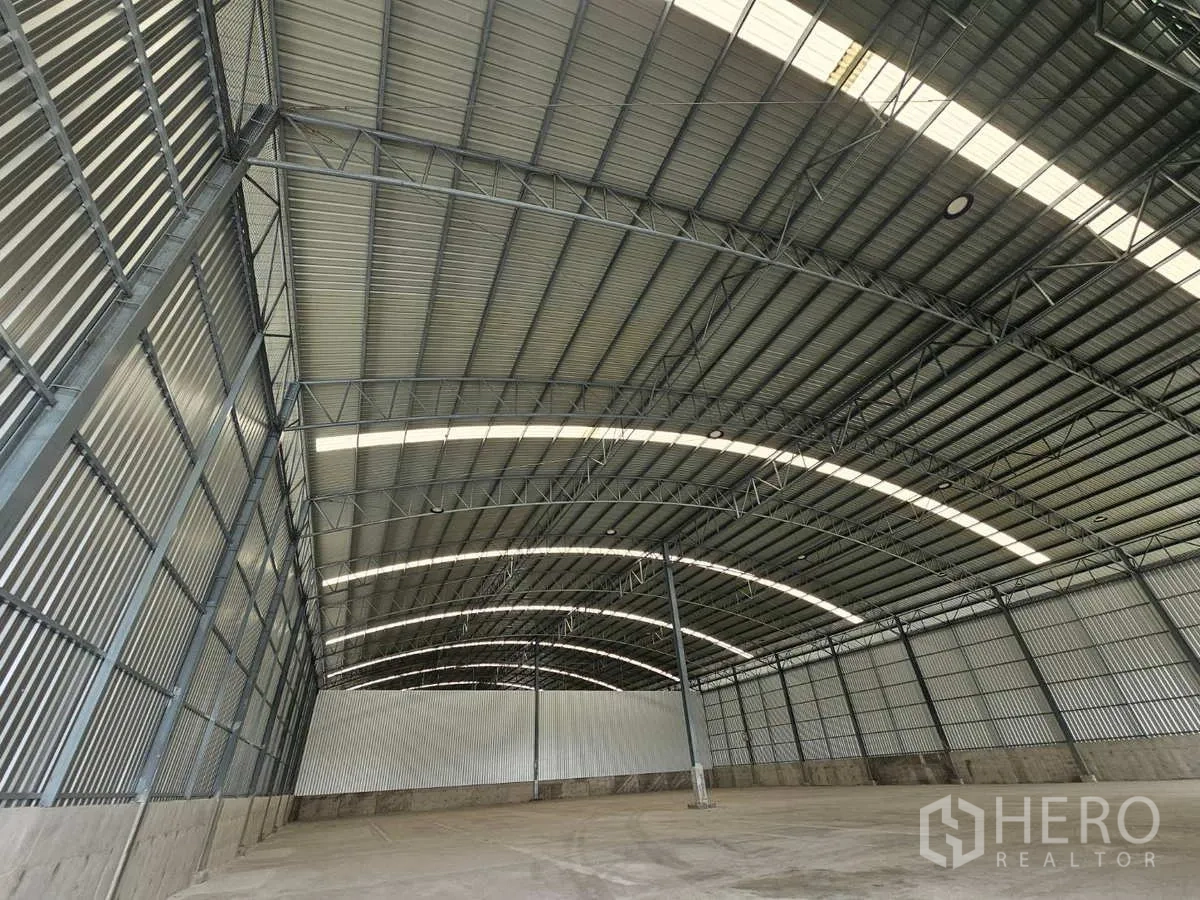 Warehouse for rent in Lam Luk Ka, Pathum Thani - Curved metal roof with skylight strips and steel trusses inside the warehouse.