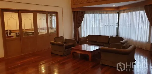 Apartment for rent in Watthana, Bangkok - Large living room with sofa set and coffee table, bay windows, and full drapes for soft natural light.