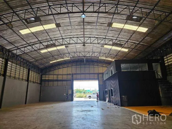 Warehouse for rent or sale in Khlong Toei, Bangkok - View toward a large roller shutter entrance with an internal two-storey black office block inside the warehouse.