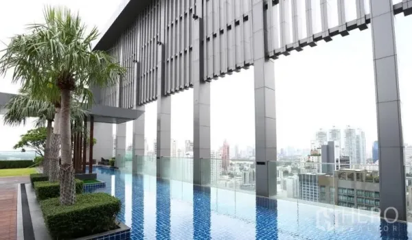 Condominium for rent or sale in Khlong Toei, Bangkok - Rooftop infinity pool with city skyline views, palm trees, and glass balustrade at a Khlong Toei condominium.