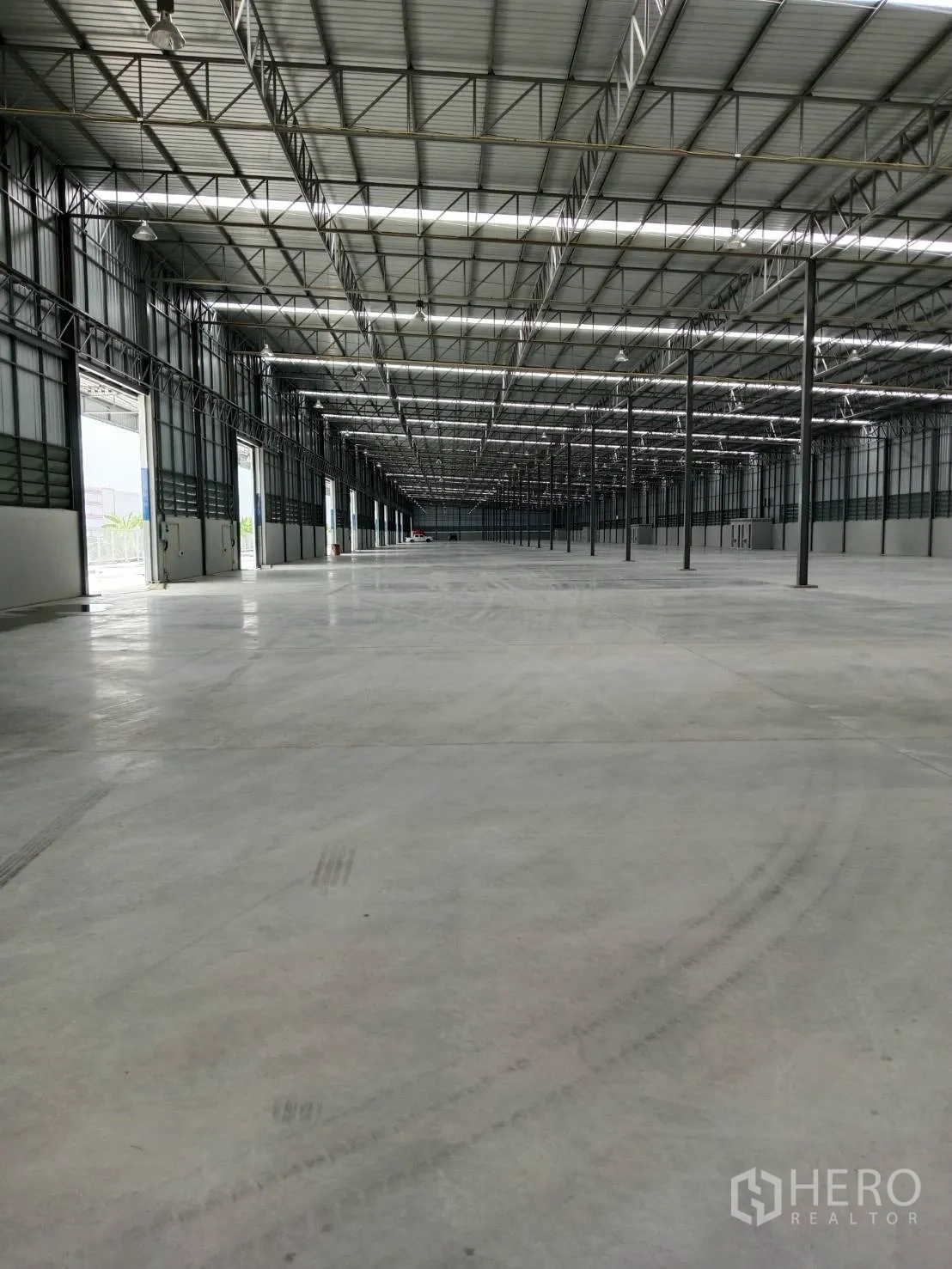 Warehouse for rent in Lat Krabang, Bangkok - Open-plan warehouse interior with concrete floor, high steel truss roof, skylight strips, and multiple access doors.
