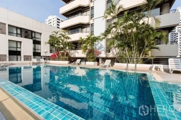 Condominium for rent in Khlong Toei, Bangkok - Outdoor swimming pool with sun loungers, palm trees and the condominium facade.