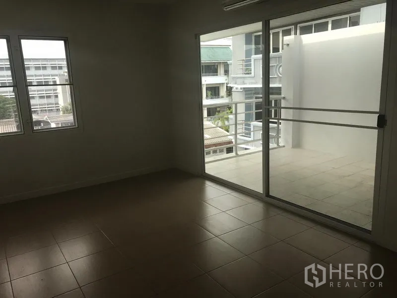 带办公室的家 出租或出售在Watthana, Bangkok - 带瓷砖地面的房间，通过推拉落地门通往宽敞阳台，可见低层社区景观。