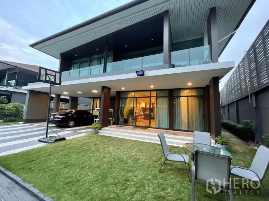 独立式住宅 出租或出售在Bang Kapi, Bangkok - 曼谷Bang Kapi现代两层独栋别墅，玻璃阳台、草坪与有顶车棚（黄昏）。