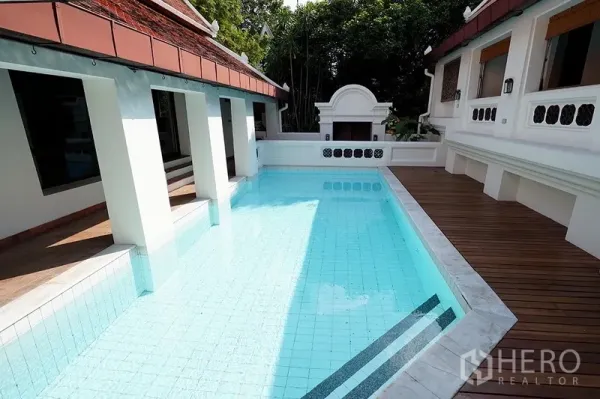 独立式住宅 出租在Watthana, Bangkok - 私人泳池铺浅蓝色瓷砖，白色围墙与木质露台环绕于别墅两翼之间。