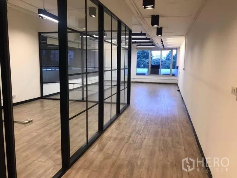 Office Space for rent in Khlong Toei, Bangkok - Open-plan office with a glass-partition meeting room, wood floors, track lighting, and wide windows.