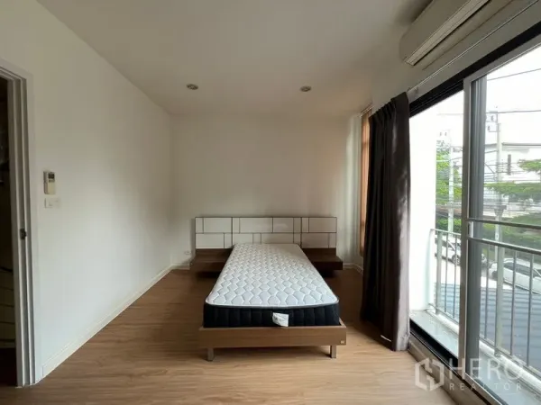 Townhouse for rent in Bang Kapi, Bangkok - Master bedroom with bed, sliding glass doors to small balcony and air-conditioner.