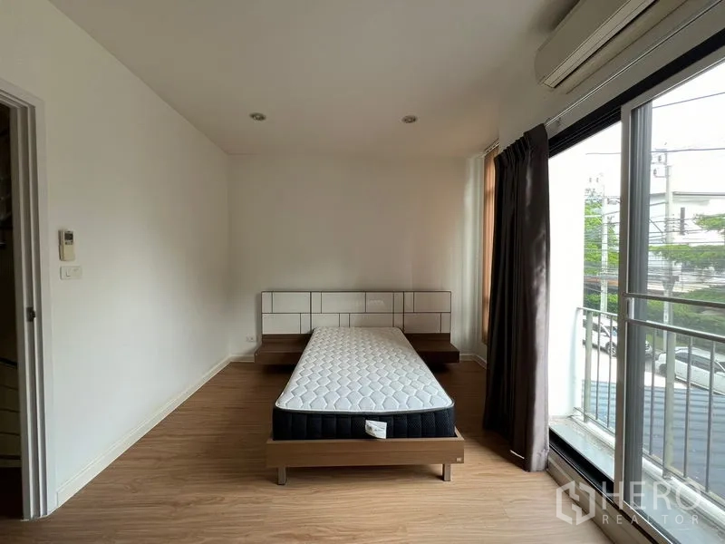 Townhouse for rent in Bang Kapi, Bangkok - Master bedroom with bed, sliding glass doors to small balcony and air-conditioner.