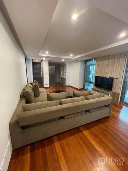 公寓 出租在Khlong Toei, Bangkok - 宽敞客厅，L形沙发，温润木地板，嵌灯天花与电视墙。