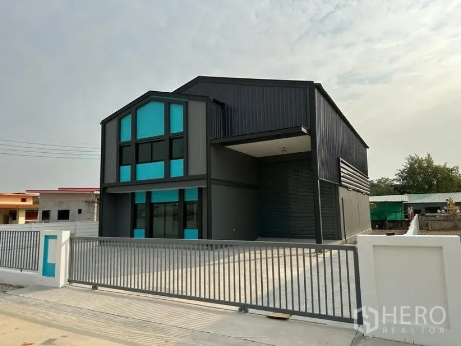 Factory for rent or sale in Bang Bua Thong, Nonthaburi - Angled exterior of the factory showing covered loading bay, large shutter door and spacious concrete driveway.