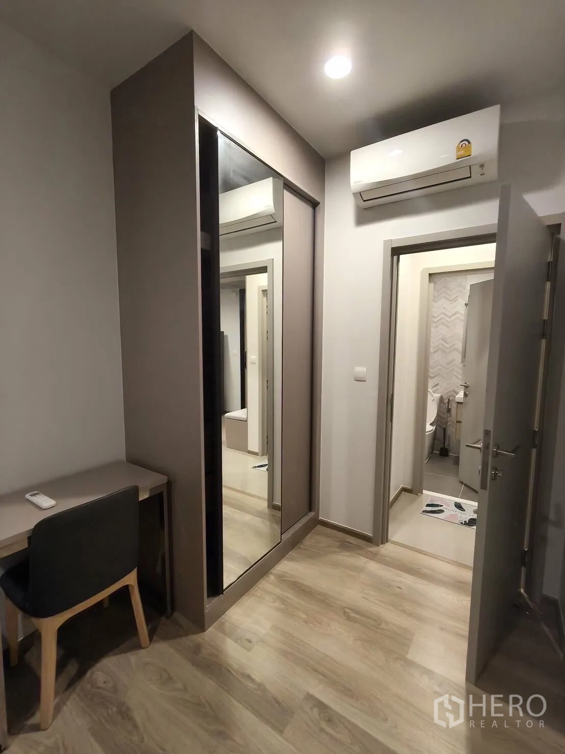 Condominium for rent in Khlong Toei, Bangkok - Second bedroom corridor with built-in desk, sliding mirrored closet, air conditioner, and a door to the bathroom.