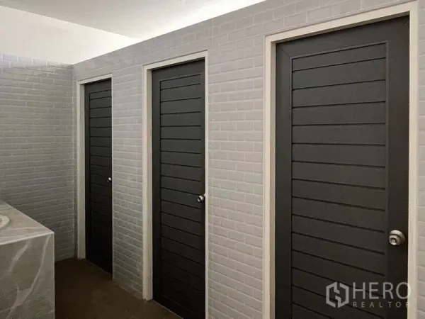 Warehouse for rent or sale - Clean tiled restroom area with three dark grey stall doors and a countertop sink.