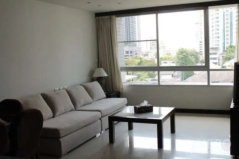 Condominium for rent in Sathon, Bangkok - Sunlit living room with large windows, sectional sofa, coffee table, and skyline outlook.