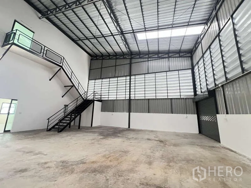 Warehouse for rent or sale - Interior bay with mezzanine stairs, ventilated cladding and a big roller shutter door.