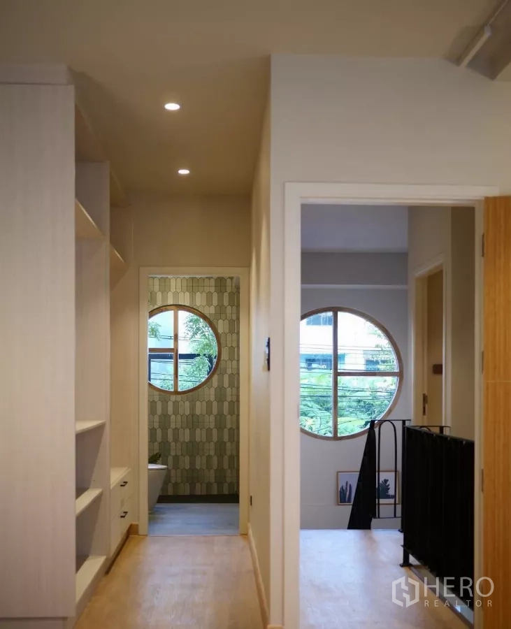 Townhouse for rent in Watthana, Bangkok - Upstairs hallway with circular windows, built-in shelving and a glimpse into the bathroom.