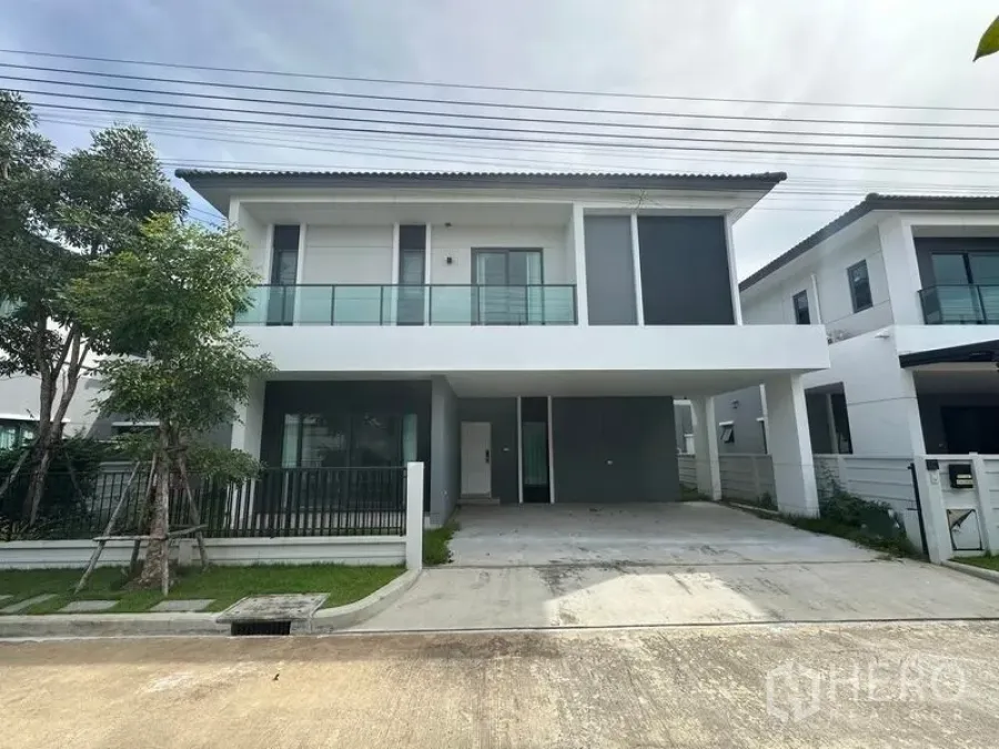 Detached House for sale in Nonthaburi - Modern two-storey detached house exterior with glass balcony and wide driveway under a covered carport.