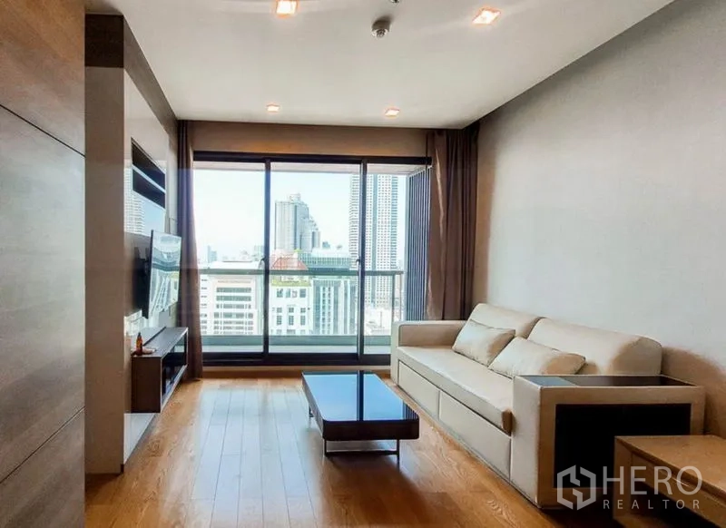 Condominium for rent in Bang Rak, Bangkok - Living room with sofa and TV console facing balcony and skyline outlook.