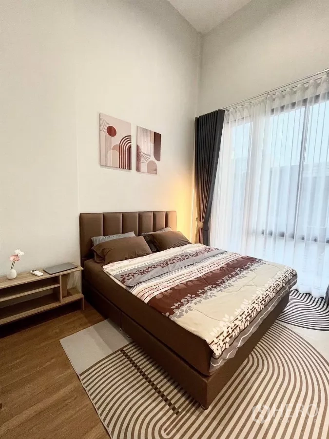 Townhouse for rent in Samut Prakan - Primary bedroom with large window, sheer curtains and queen bed.