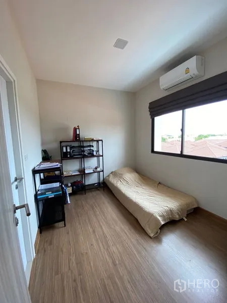 Townhouse for rent in Suan Luang, Bangkok - Guest bedroom with single bed, shelving unit and window air conditioning.