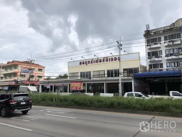 Retail Space for rent in Lam Luk Ka, Pathum Thani - Angled view of the retail block along a busy roadway with cars, grass median and neighboring shophouses.