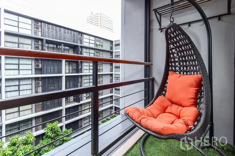 Condominium for rent in Watthana, Bangkok - Private balcony featuring a rattan hanging egg chair with orange cushion overlooking the courtyard.