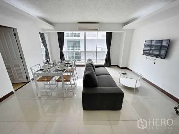 Condominium for rent in Khlong Toei, Bangkok - Bright open-plan living and dining area with sofa, wall-mounted TV and large windows to the balcony.