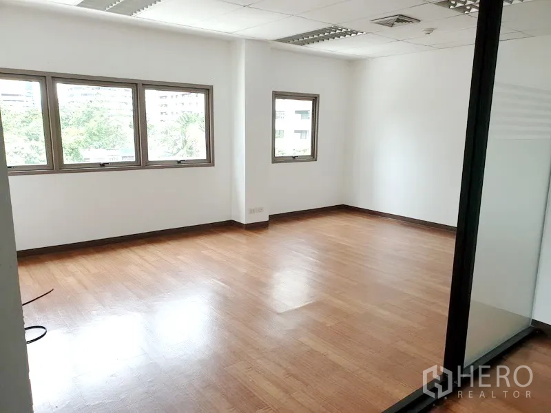 Office Space for rent in Khlong Toei, Bangkok - Private office room with wood floors, white walls, several windows overlooking greenery, and grid ceiling lighting.
