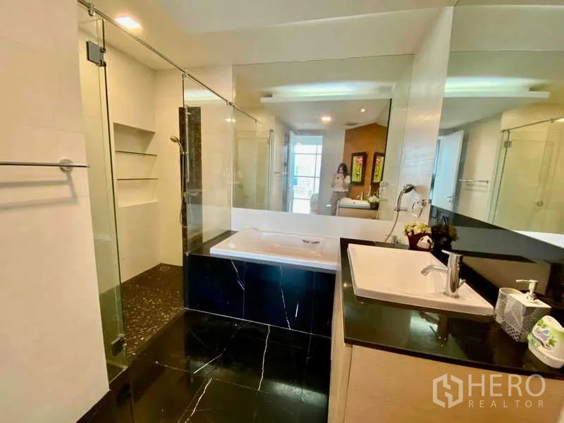 Condominium for rent or sale in Sathon, Bangkok - Master bathroom with glass shower, soaking tub, and long vanity mirror.