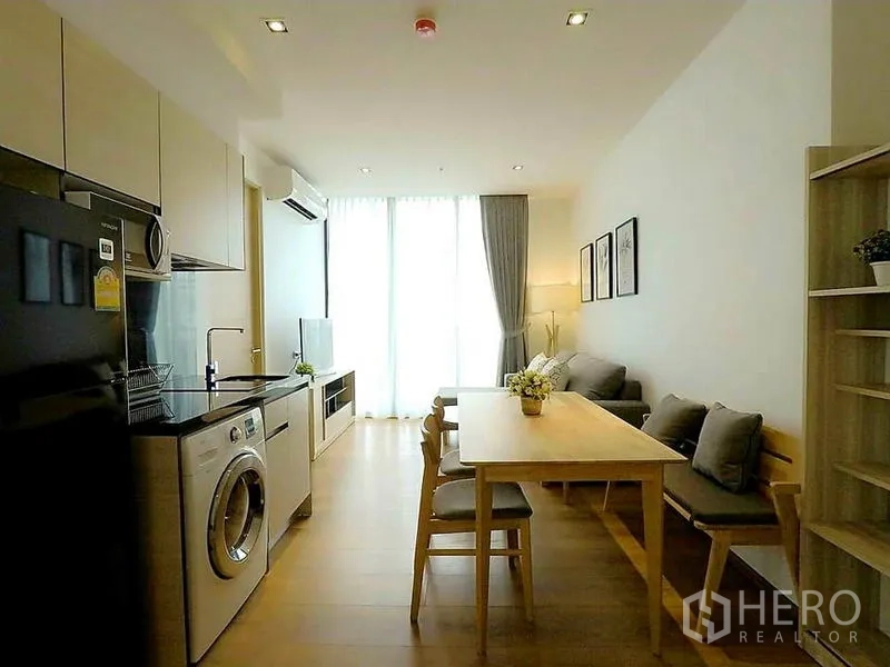 Condominium for rent in Khlong Toei, Bangkok - Streamlined galley kitchen with fridge and washer facing dining and living area.