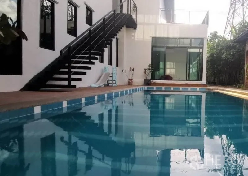 独立式住宅 出售在Pak Kret, Nonthaburi - 大型泳池临白色外立面，外部楼梯与玻璃房间。