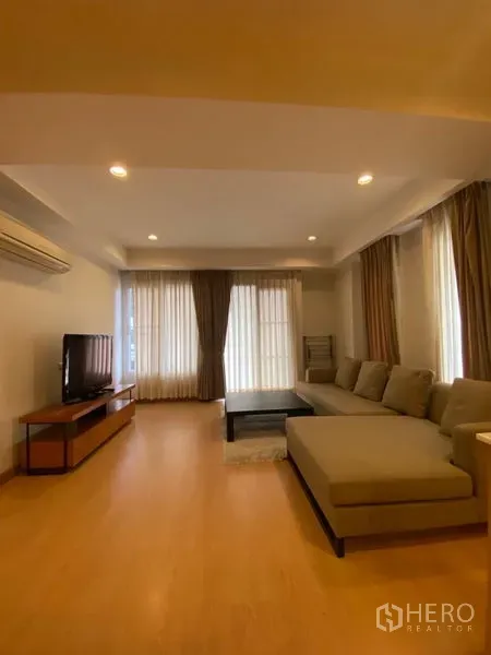 คอนโด ให้เช่าในWatthana, Bangkok - ห้องนั่งเล่นสว่าง โปร่ง โซฟารูปตัว L ชั้นวางทีวี พื้นไม้ และผ้าม่านสูงจรดเพดาน