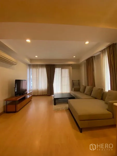 คอนโด ให้เช่าในWatthana, Bangkok - ห้องนั่งเล่นสว่าง โปร่ง โซฟารูปตัว L ชั้นวางทีวี พื้นไม้ และผ้าม่านสูงจรดเพดาน